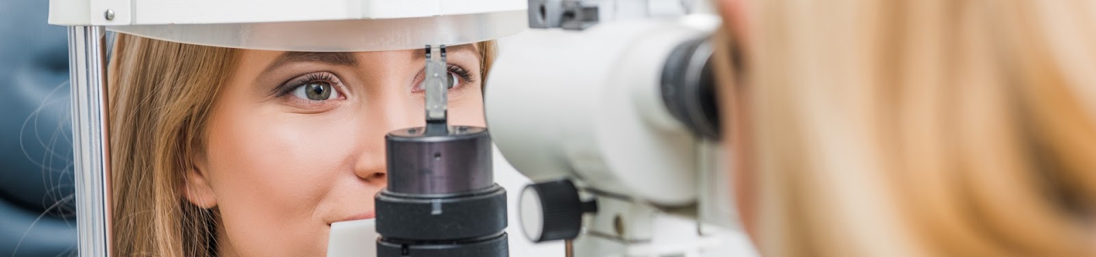 Smiling young blonde woman having her eyes examined by an eye doctor as she rests her head against a vision testing machine