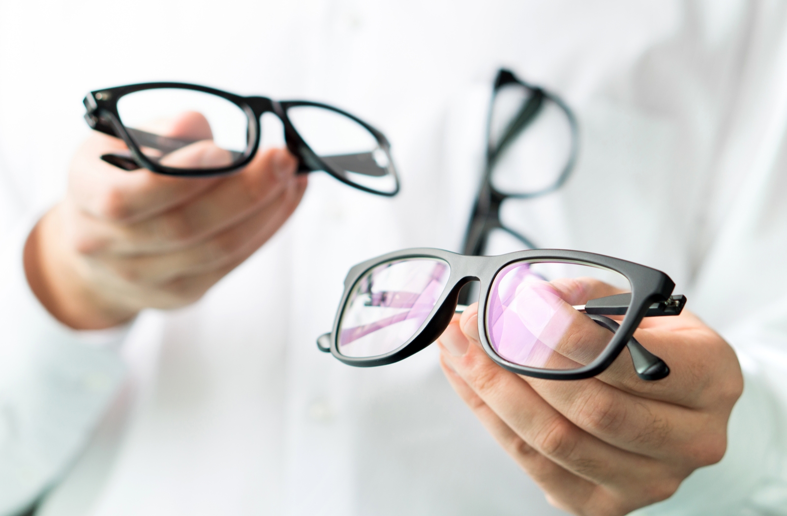 An optician holding out two pairs of glasses with different lens coatings
