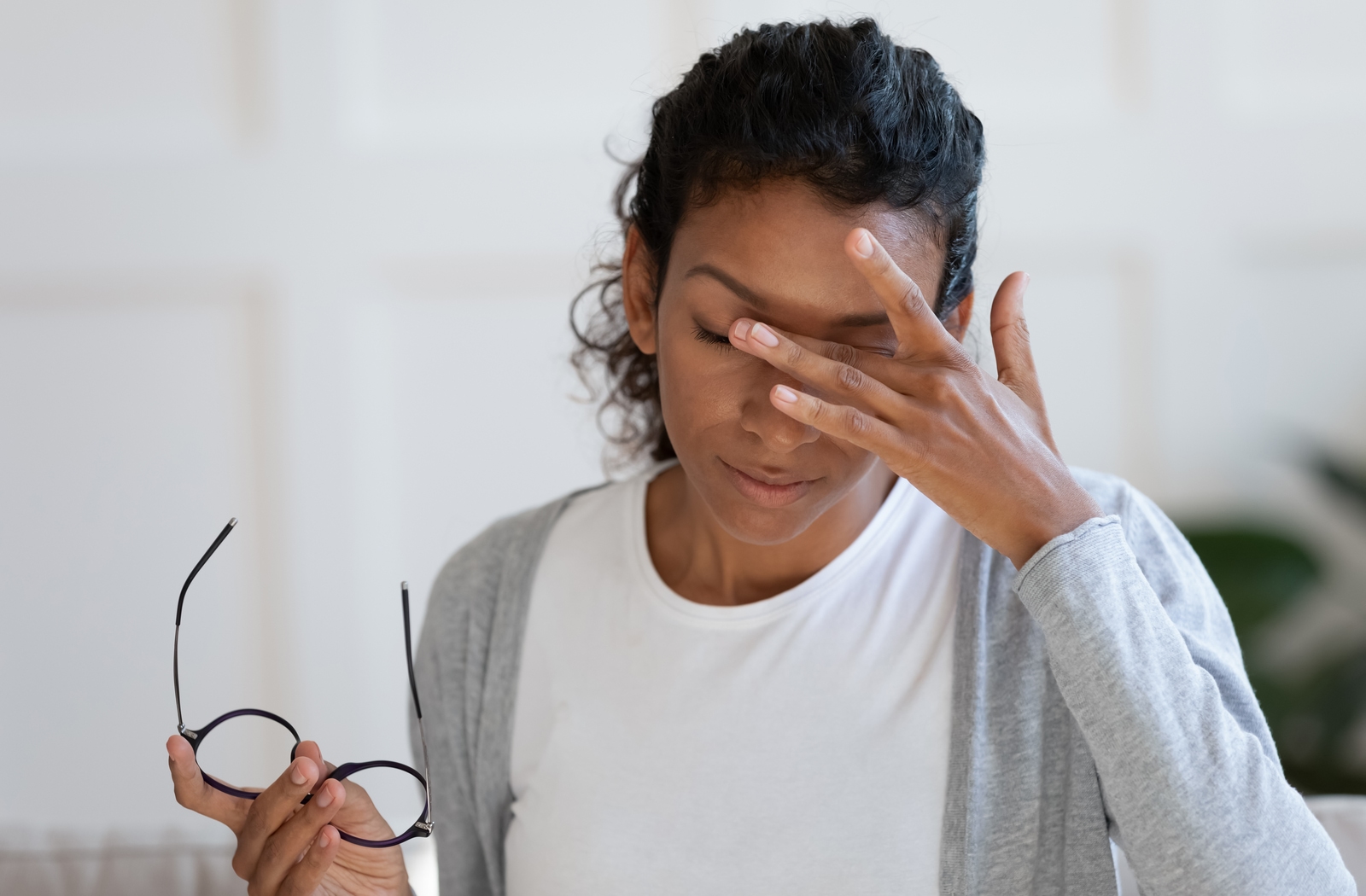 A woman taking off her glasses holding her eye's in discomfort due to dry eye going untreated