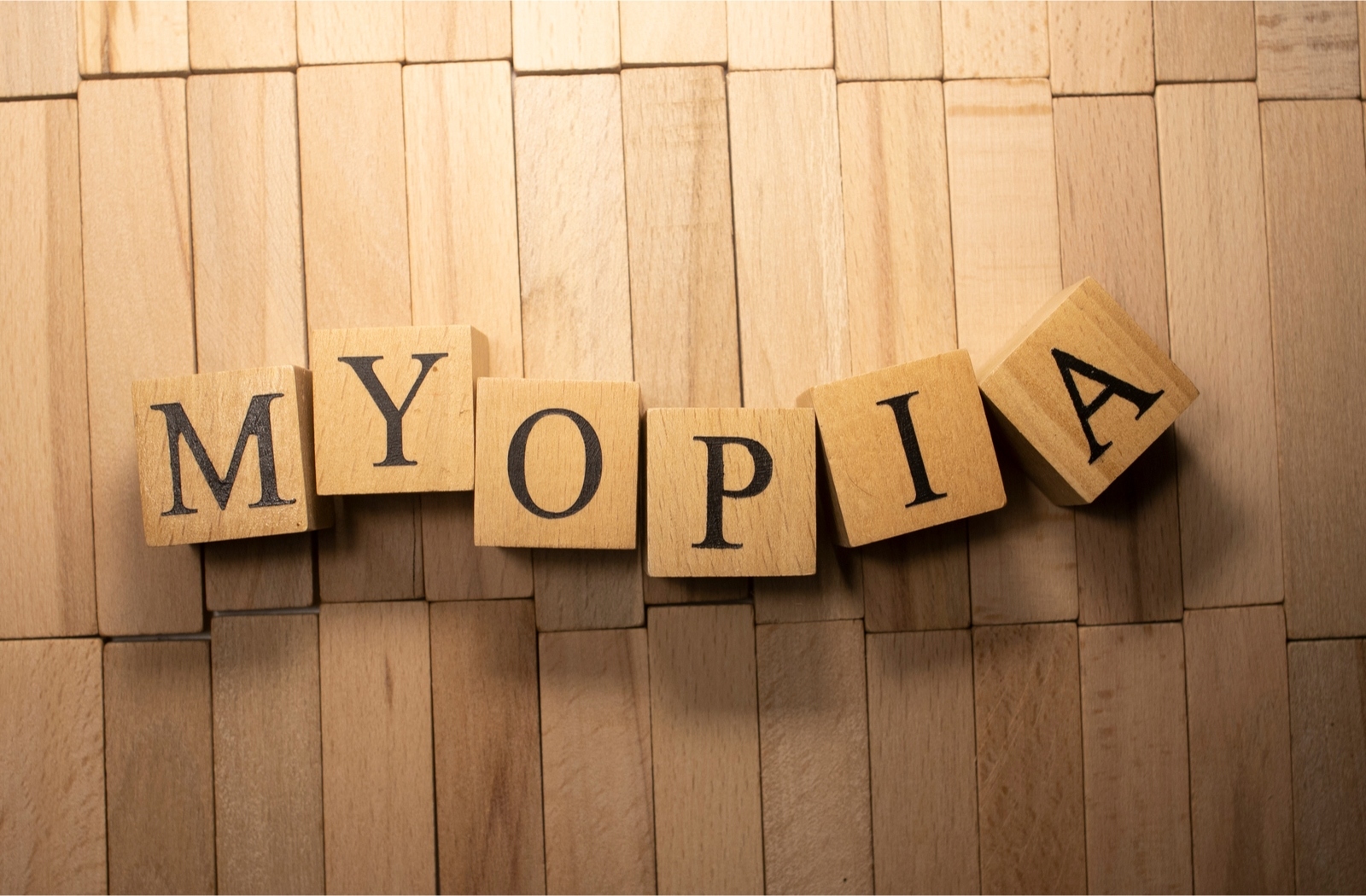 The word Myopia spelled out in wooden block letters arranged against a wall of small wood slats.