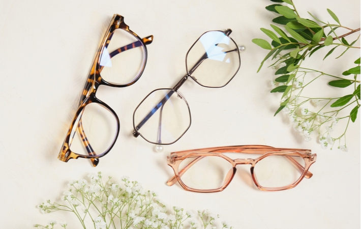 Three glasses with different colours and styles placed on a beige background surrounded by flowers