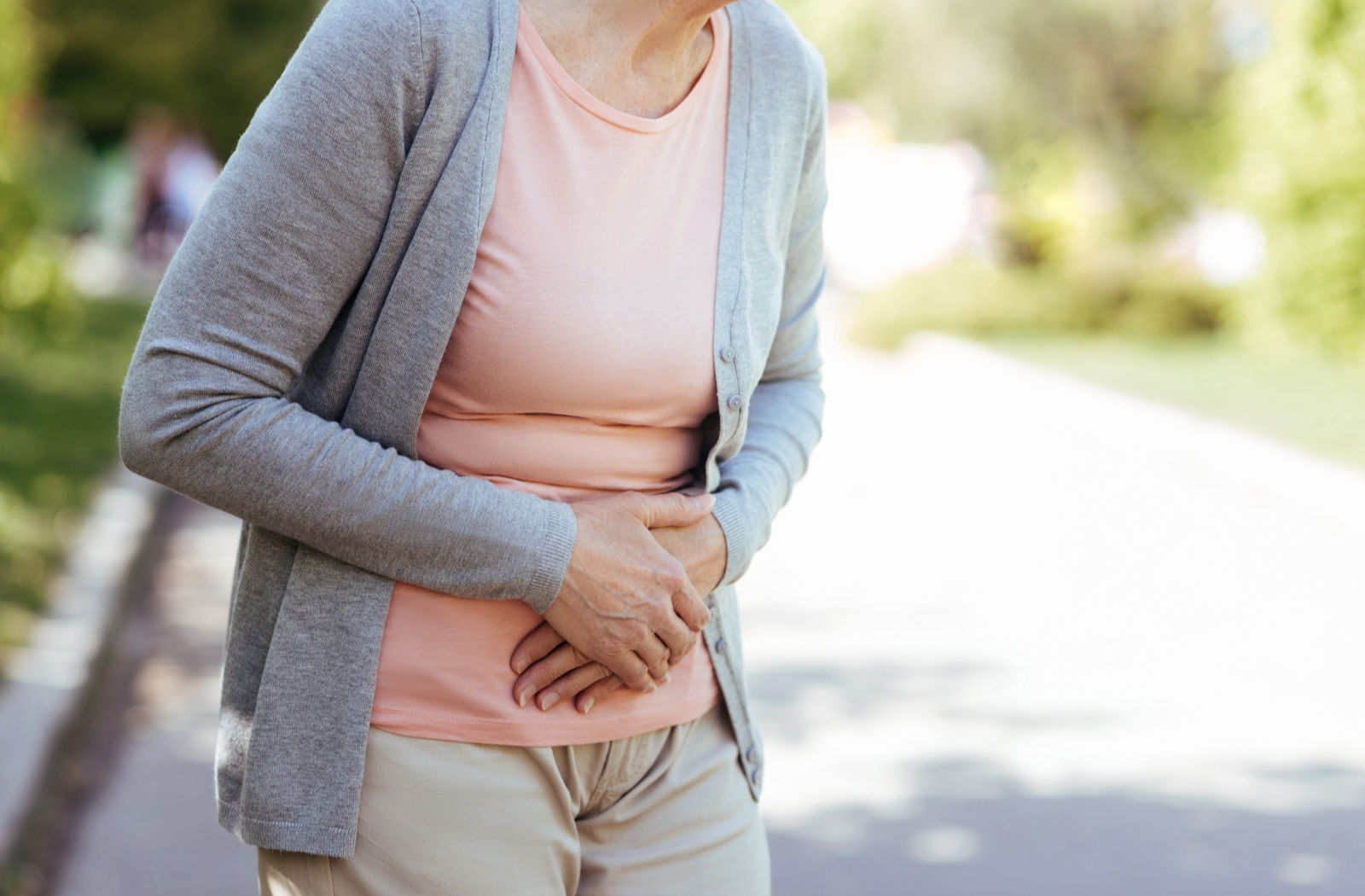 An older woman with her hands over her stomach due to stomach pain
