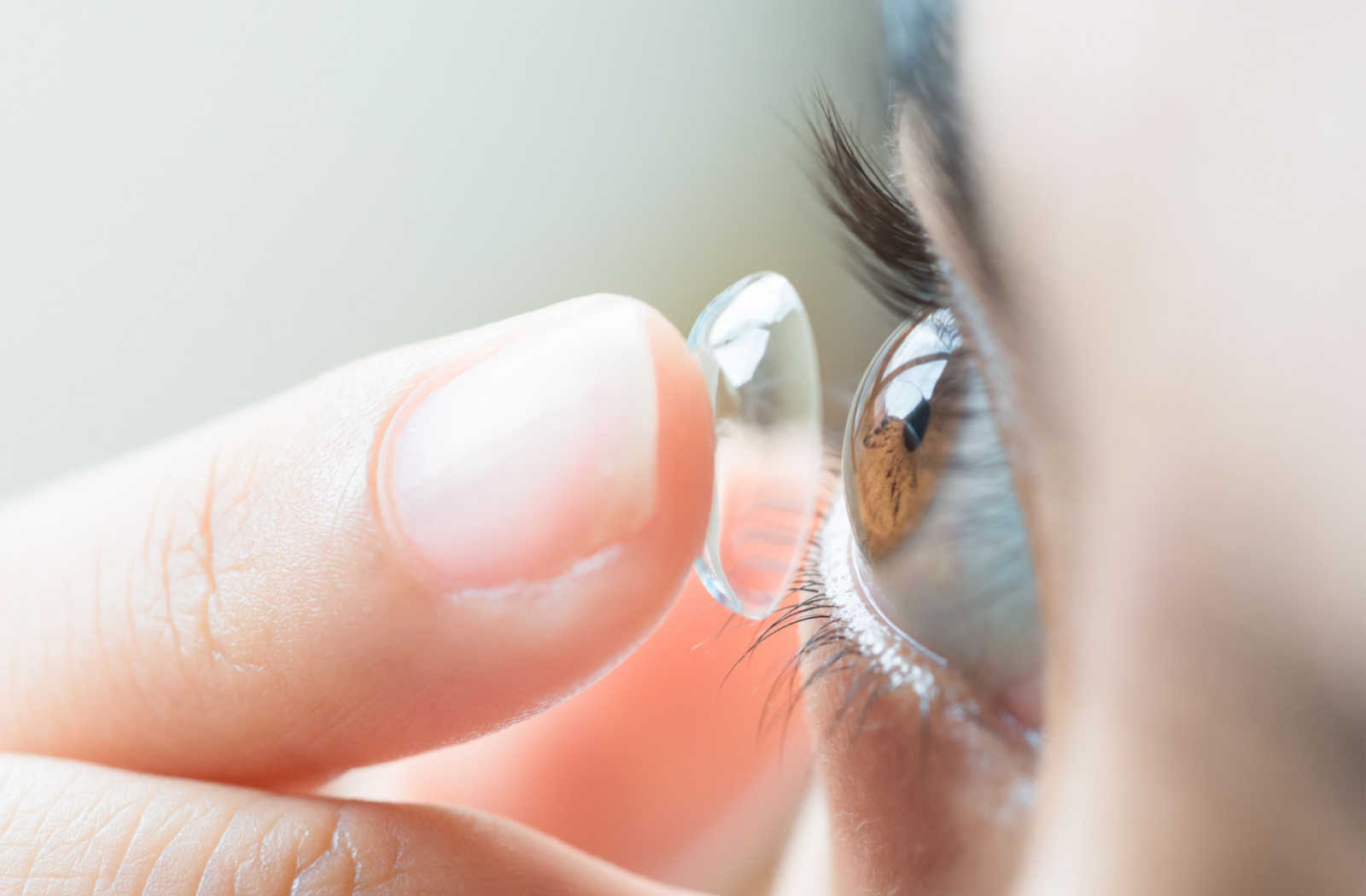 A close up of a scleral lens on a finger being applied to the eye.