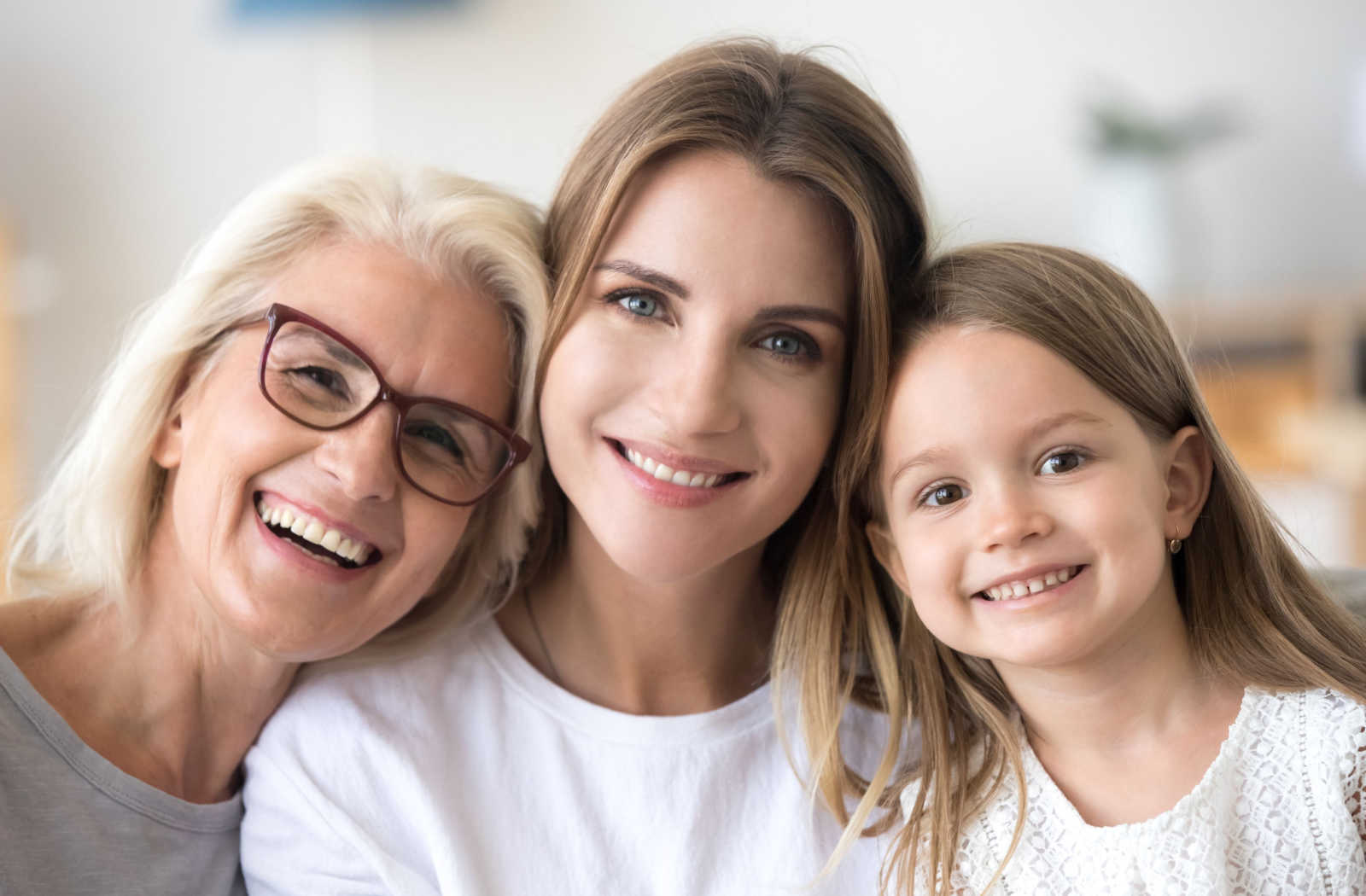 A grandmother wearing glasses, daughter, and granddaughter all smiling.
