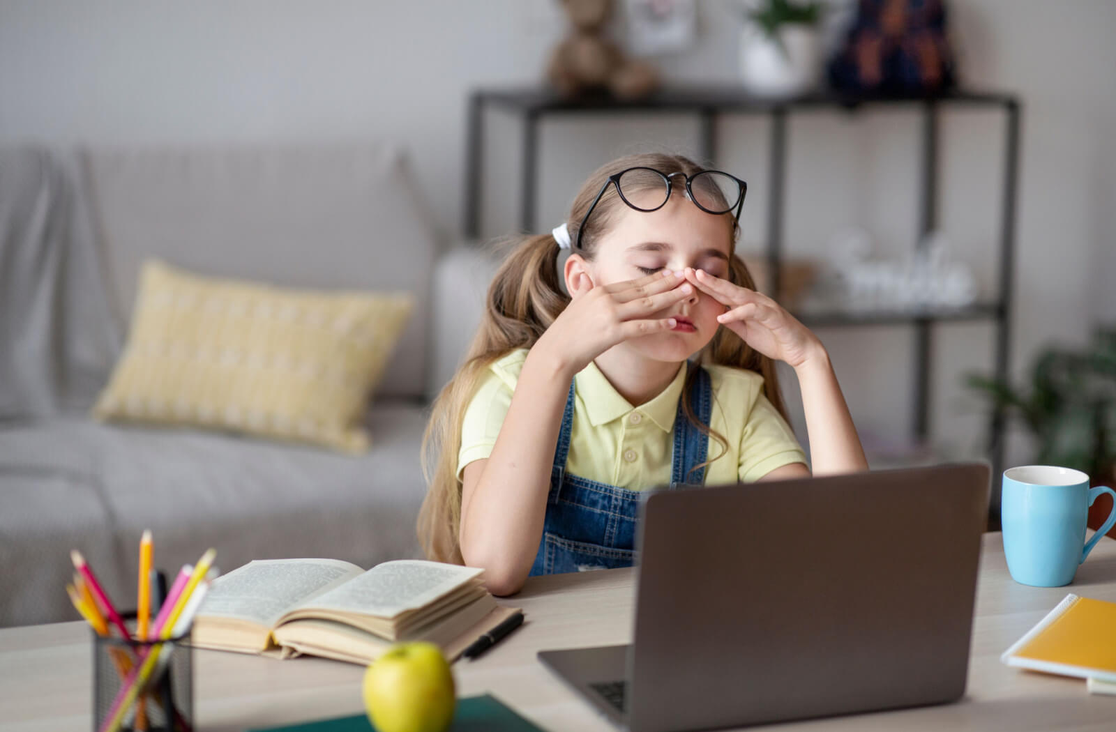A female child sitting in front of her computer is massaging her eyes to relax after a long period of staring at the screen.