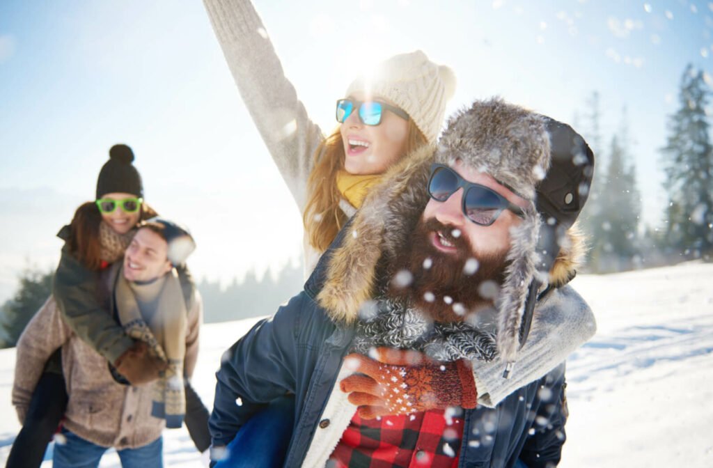 A group of two couples are wearing winter clothes and sunglasses while enjoying he snow outdoors