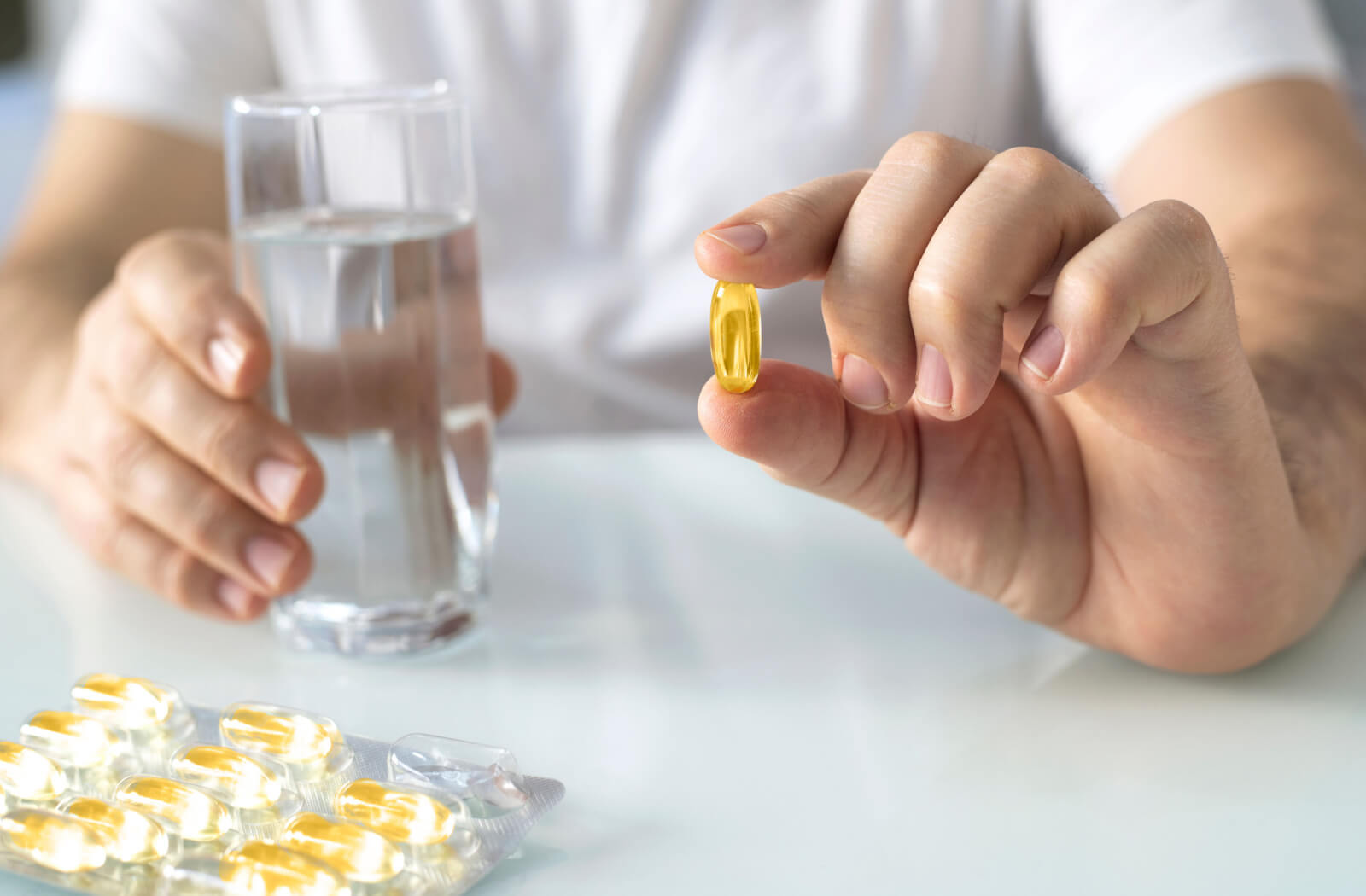 A close-up of a man's hands holding omega-3 fish oil and a glass of water.