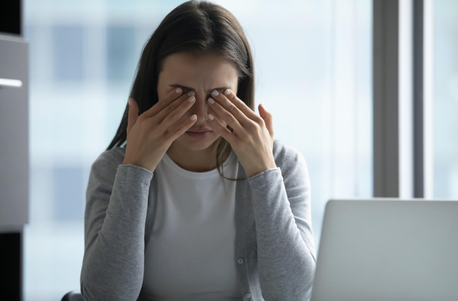 A young woman sitting in front of her computer is massaging her eyes, suffering from dry eyes and experiencing blurry vision.