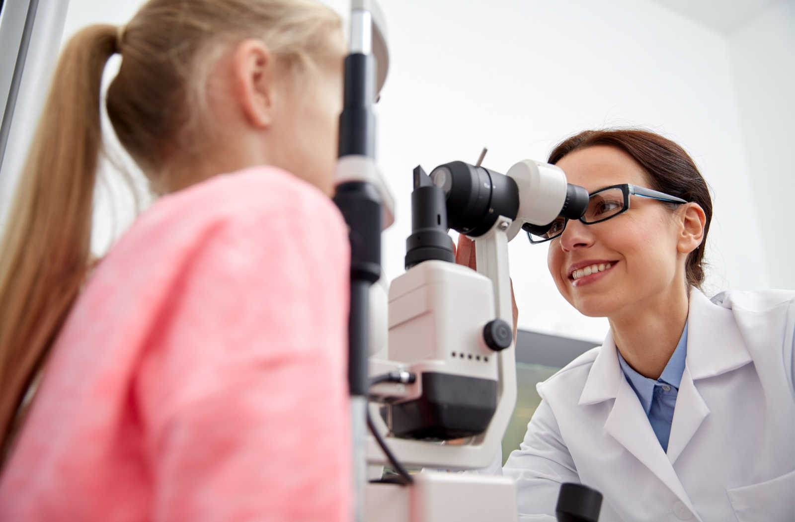 A female optometrist examines a young girls eyes during a comprehensive kids eye exam.