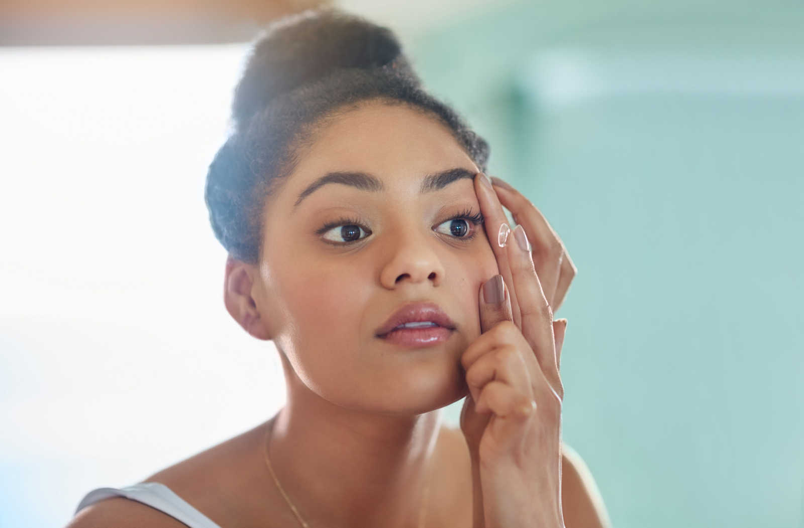 A woman looking in the mirror holding her eye in order to put her contact lenses in.
