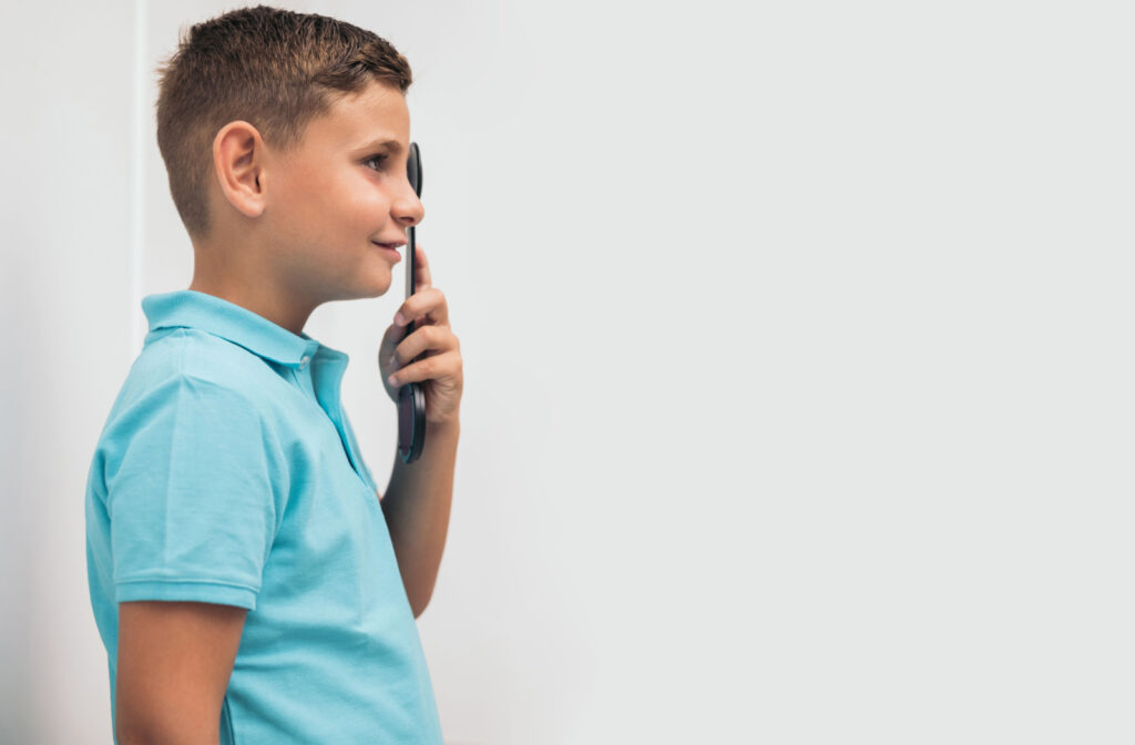 A young boy in the middle of an eye exam holding a black occluder.