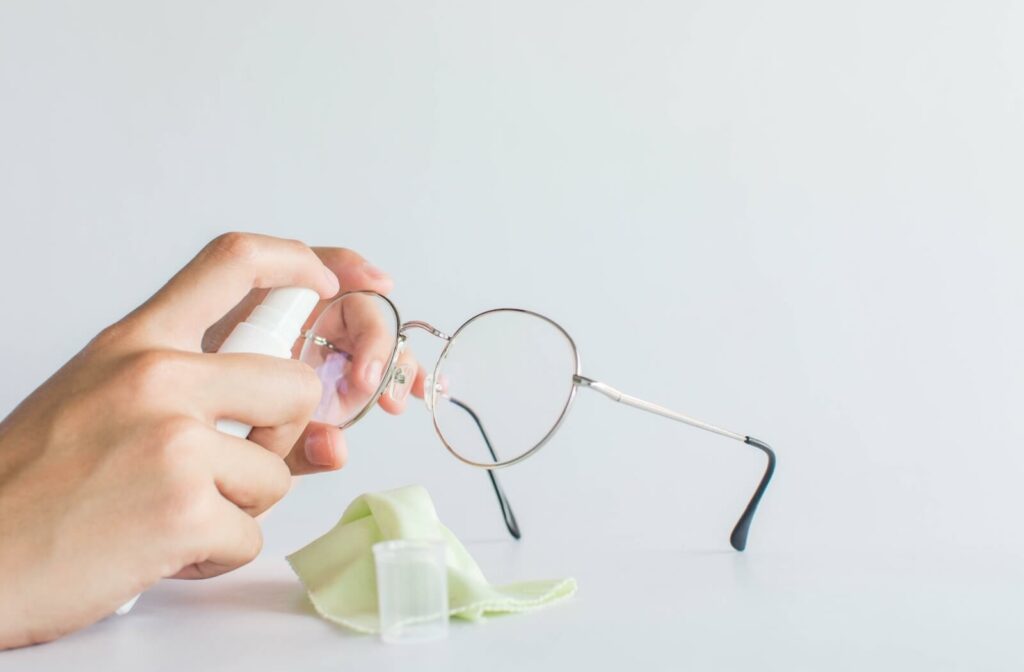 A person uses a cleaning spray and a microfiber cloth to clean and care for their eyeglasses.