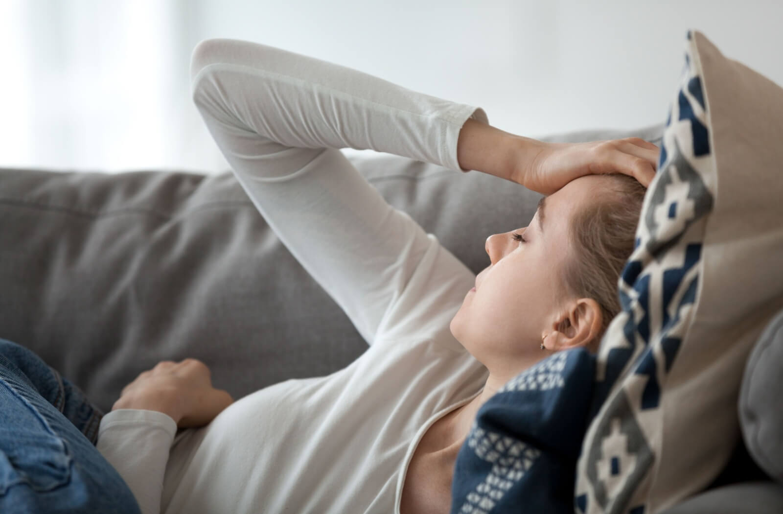 A young adult with a tension headache lies on a couch and presses their palm into their forehead.