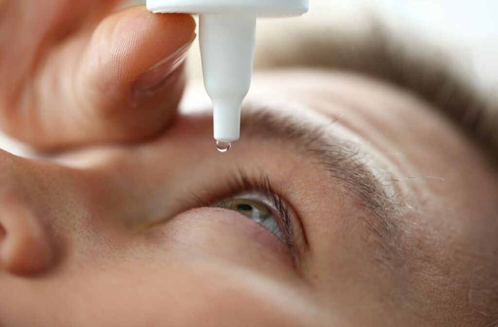 An adult opens their eyes and looks up as they gently squeeze some eye drops into their eyes for dry eye relief.