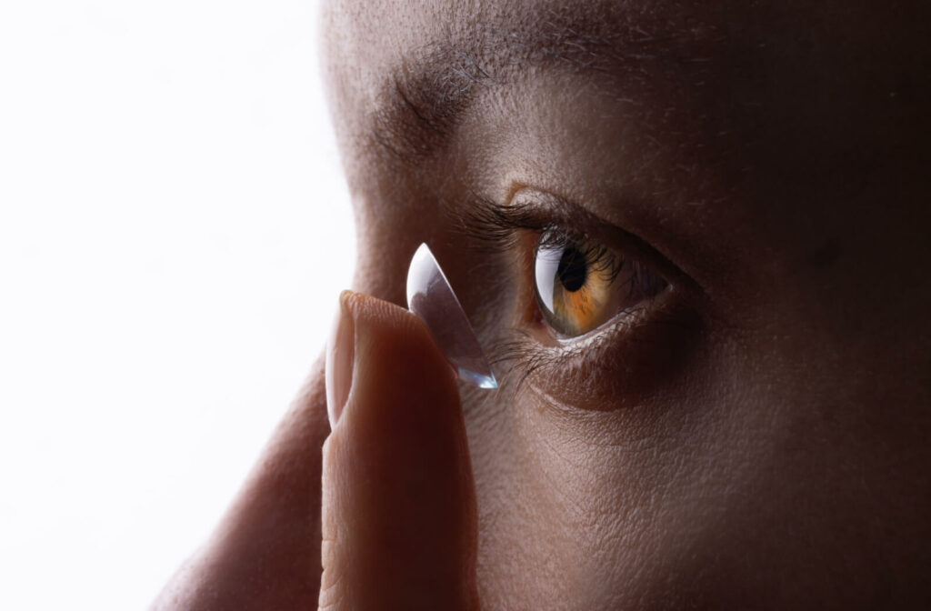 Close-up of a person inserting a contact lens onto their brown eye.